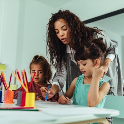Little girls painting with a teacher in preschool