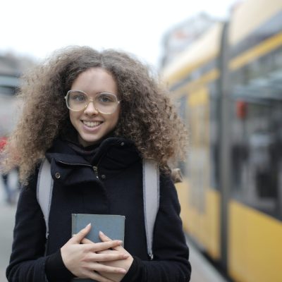 cheerful-young-lady-in-eyeglasses-standing-on-street-with-3974063